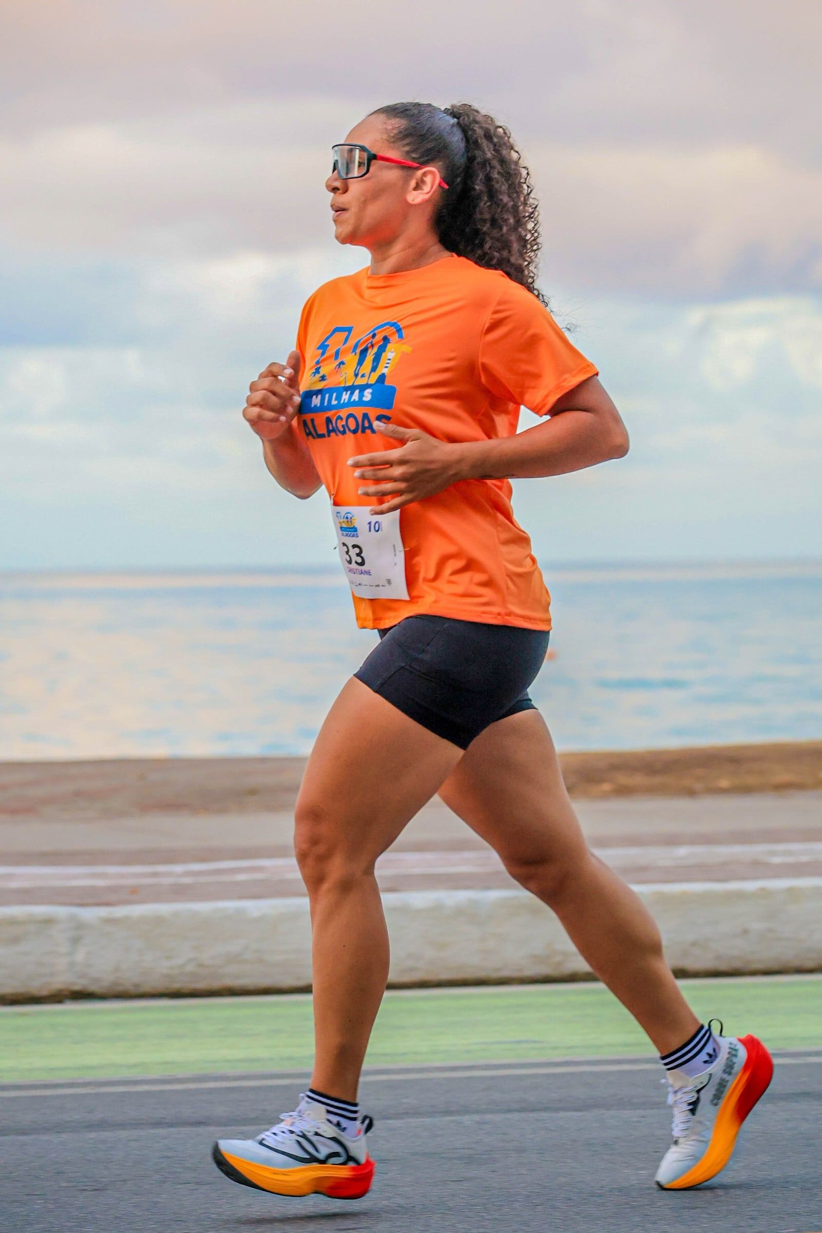Corredora com a camisa oficial laranja na orla, com o mar ao fundo